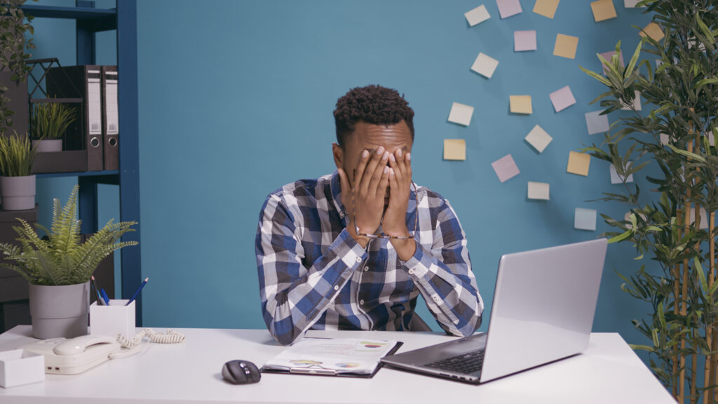 Frustrated worker feeling exhausted about office work, using laptop computer at desk. Tired employee working on business plan, feeling angry and disappointed about financial mistake.