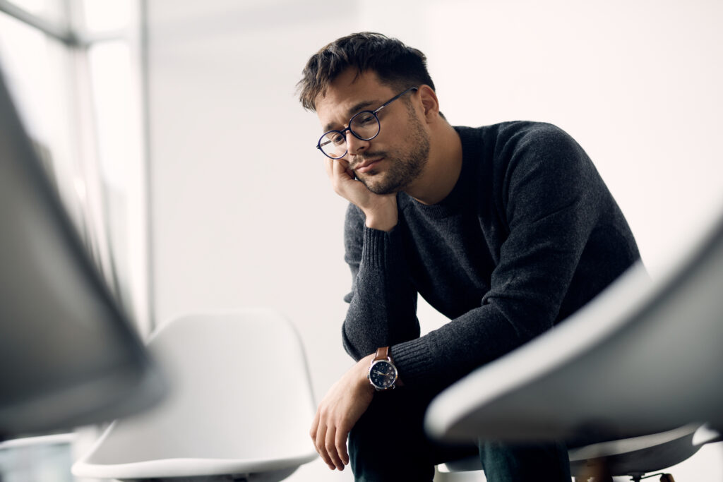 Young worried man sitting in a chair and thinking while waiting a group therapy to start.