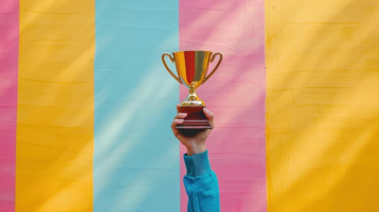 Hand Holding Golden Trophy Against Colorful Wall | Tbelle